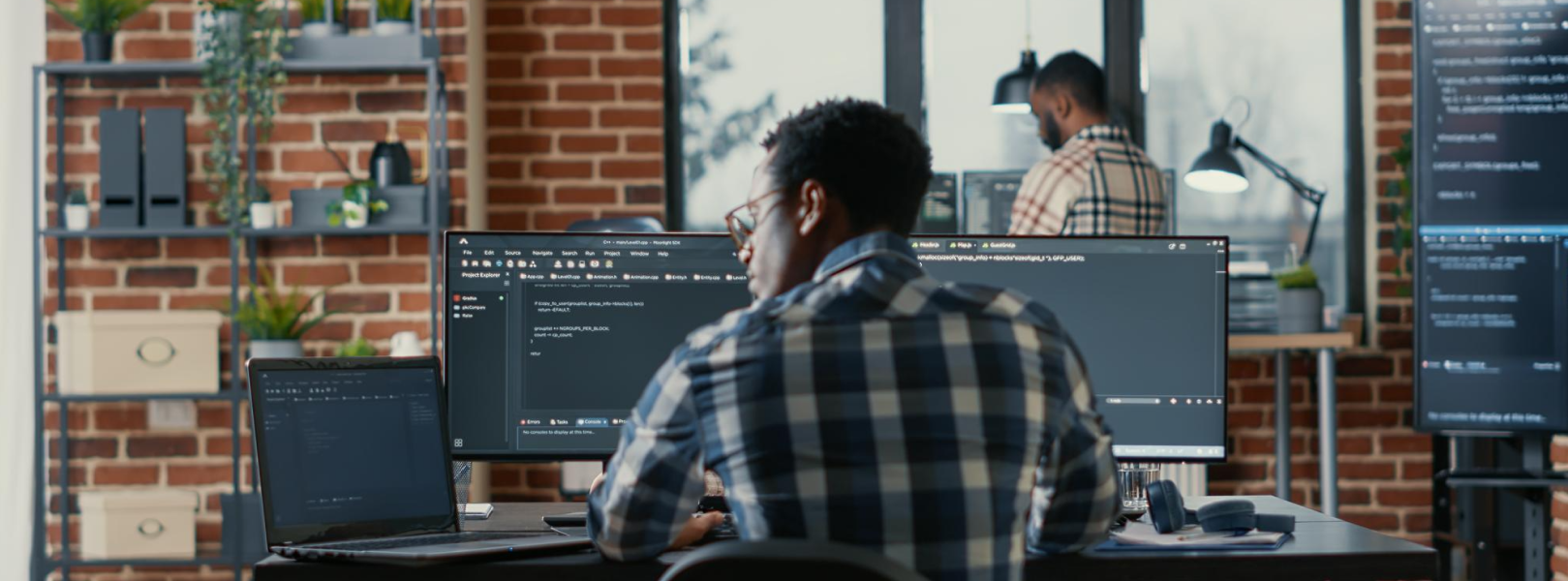 a man working on software development outsourcing in front of three screens.